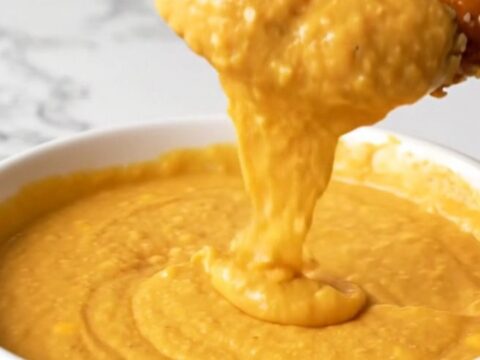 A bowl of creamy, melted beer cheese dip served with soft pretzel bites on a rustic wooden table.