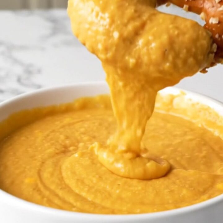 A bowl of creamy, melted beer cheese dip served with soft pretzel bites on a rustic wooden table.