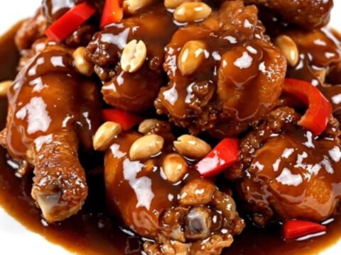 A close-up of glossy Kung Pao chicken with peanuts and peppers on a white plate.