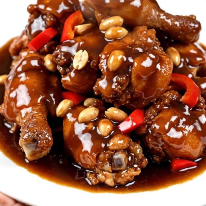 A close-up of glossy Kung Pao chicken with peanuts and peppers on a white plate.