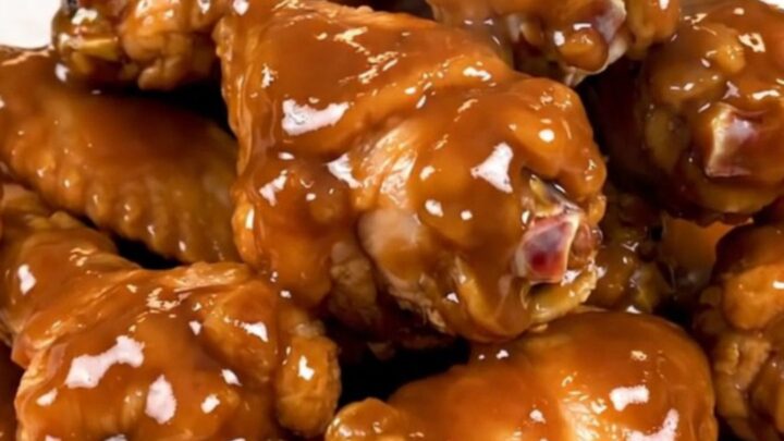 A top-down view of raw chicken wings and onions inside a black slow cooker insert.