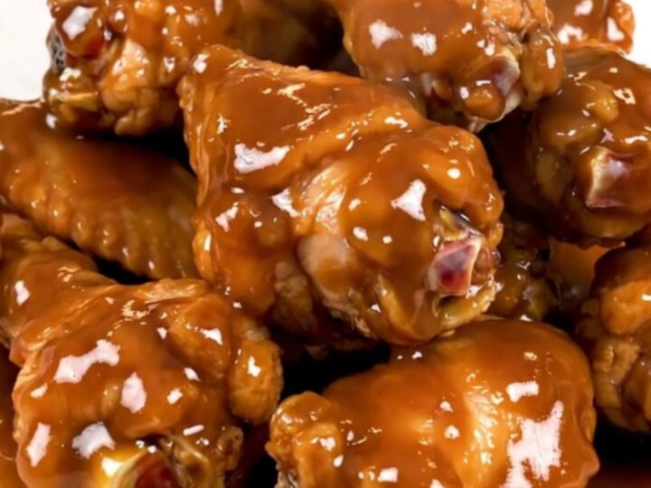 A top-down view of raw chicken wings and onions inside a black slow cooker insert.
