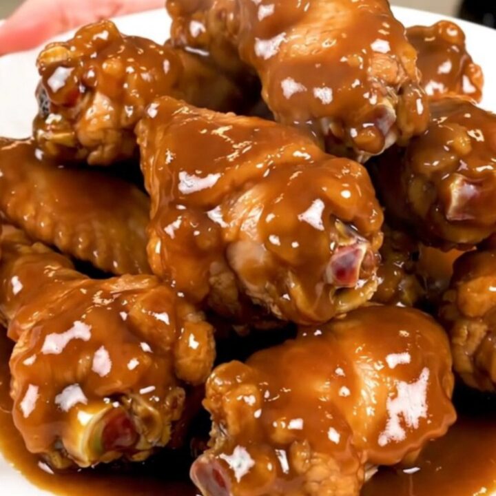 A top-down view of raw chicken wings and onions inside a black slow cooker insert.