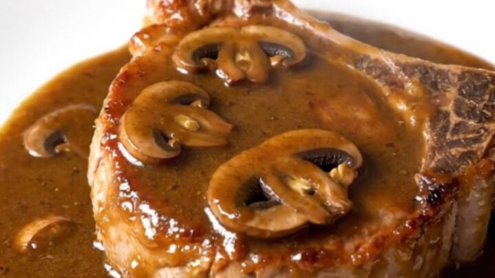 A close-up of a juicy bone-in pork chop topped with creamy mushroom gravy on a white plate.