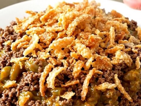 A top-down view of a black slow cooker filled with ground beef, green beans, and mushroom sauce.