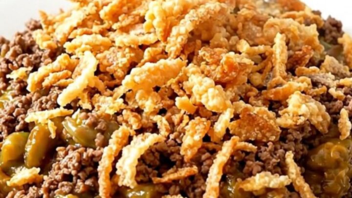 A top-down view of a black slow cooker filled with ground beef, green beans, and mushroom sauce.