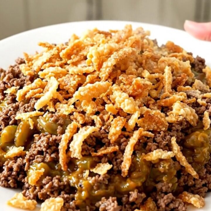 A top-down view of a black slow cooker filled with ground beef, green beans, and mushroom sauce.