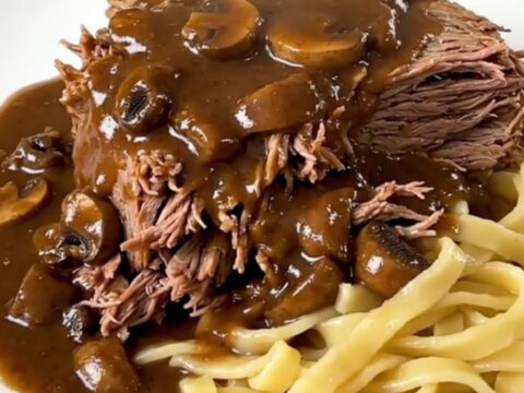 A slow cooker filled with a tender beef chuck roast covered in a rich, creamy mushroom gravy.