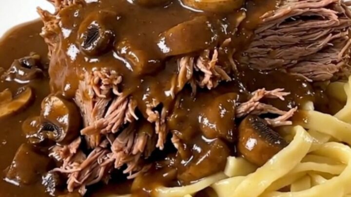A slow cooker filled with a tender beef chuck roast covered in a rich, creamy mushroom gravy.