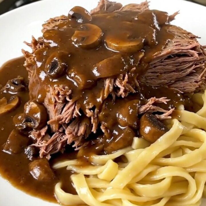 A slow cooker filled with a tender beef chuck roast covered in a rich, creamy mushroom gravy.
