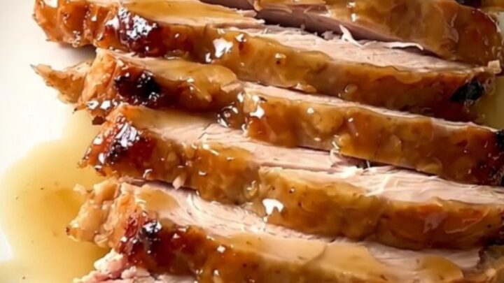 A close-up of a perfectly cooked, glazed turkey breast in a black slow cooker insert on a speckled countertop.
