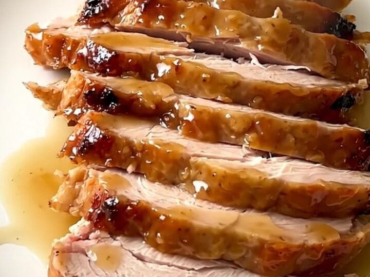 A close-up of a perfectly cooked, glazed turkey breast in a black slow cooker insert on a speckled countertop.