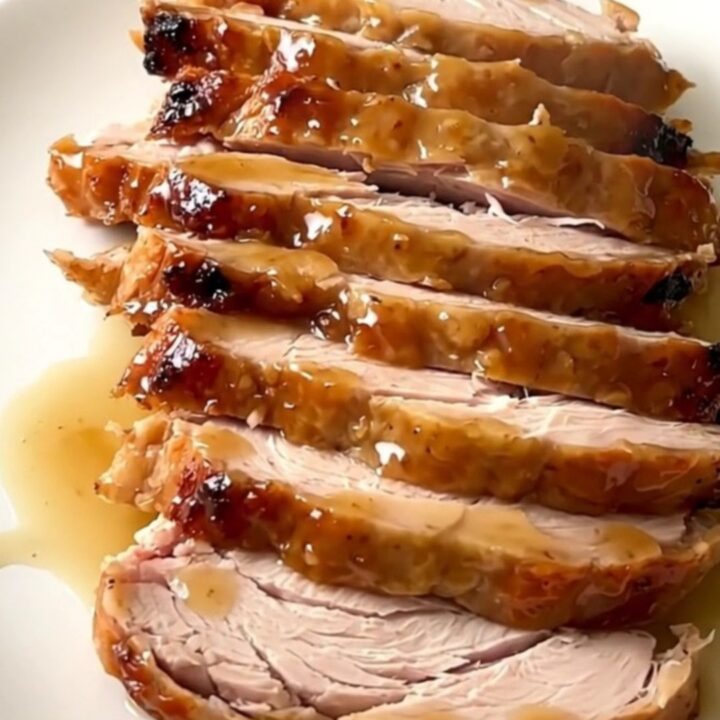 A close-up of a perfectly cooked, glazed turkey breast in a black slow cooker insert on a speckled countertop.