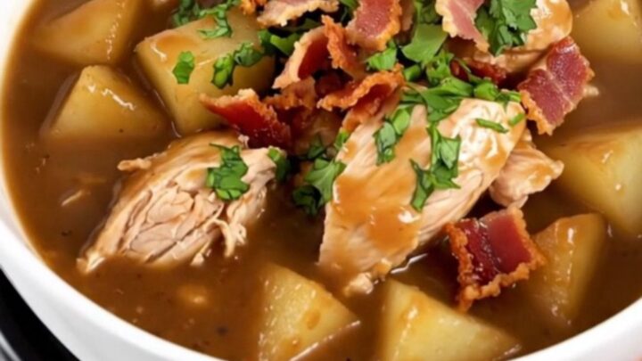 A steaming bowl of slow cooker apple bacon chicken stew garnished with crispy bacon and fresh parsley.