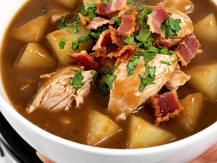 A steaming bowl of slow cooker apple bacon chicken stew garnished with crispy bacon and fresh parsley.