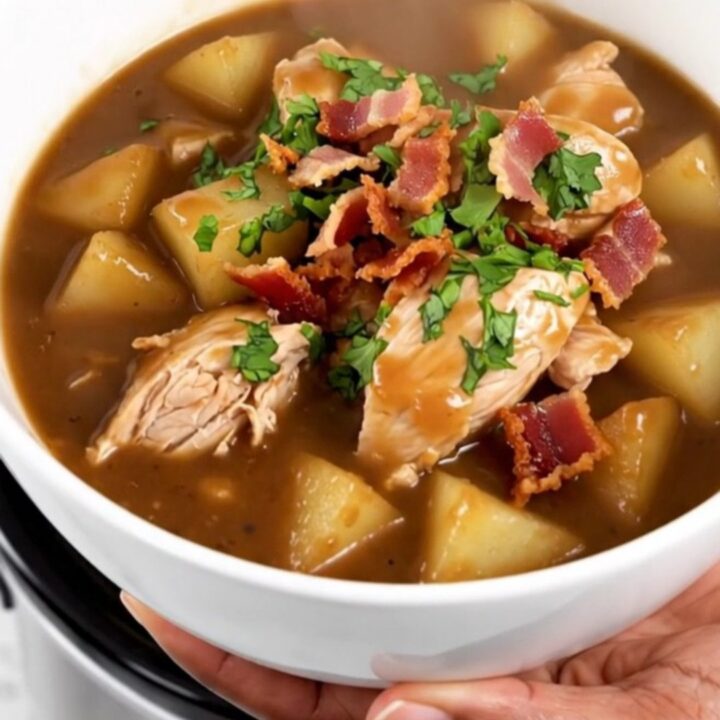 A steaming bowl of slow cooker apple bacon chicken stew garnished with crispy bacon and fresh parsley.