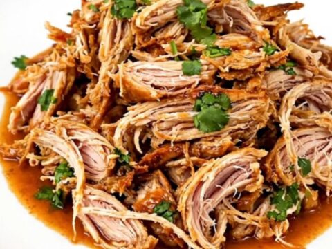 A slow cooker filled with shredded cilantro lime chicken on a white speckled countertop.