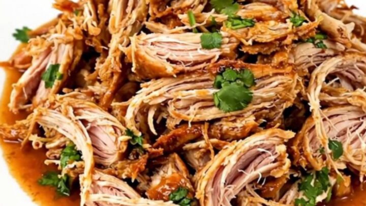 A slow cooker filled with shredded cilantro lime chicken on a white speckled countertop.