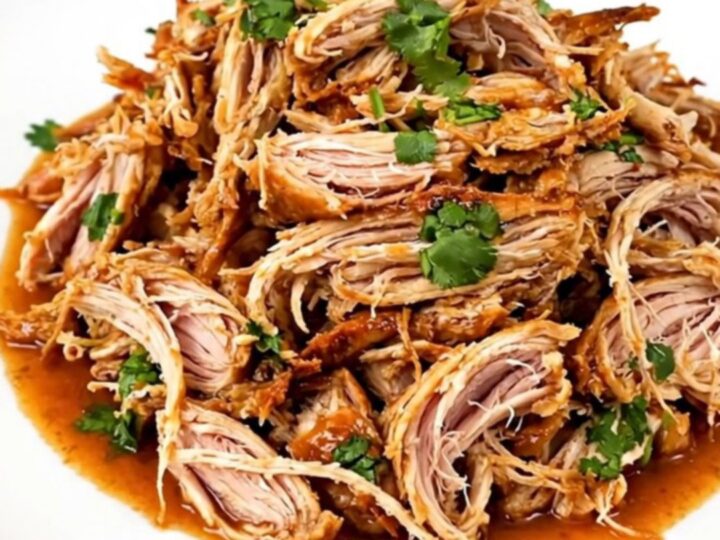 A slow cooker filled with shredded cilantro lime chicken on a white speckled countertop.