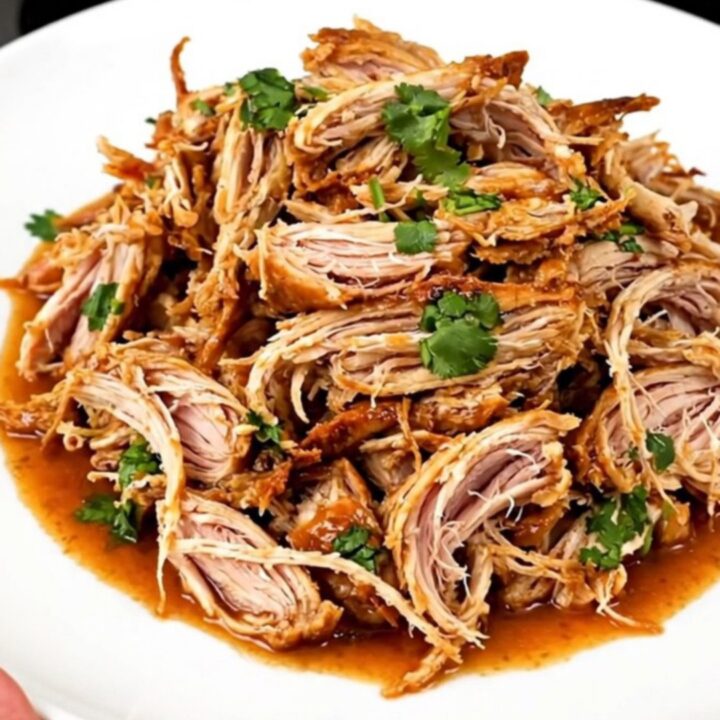 A slow cooker filled with shredded cilantro lime chicken on a white speckled countertop.