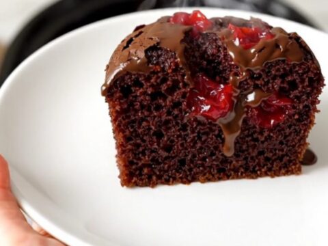 A warm, glossy chocolate cherry dump cake in a black slow cooker on a white quartz countertop.