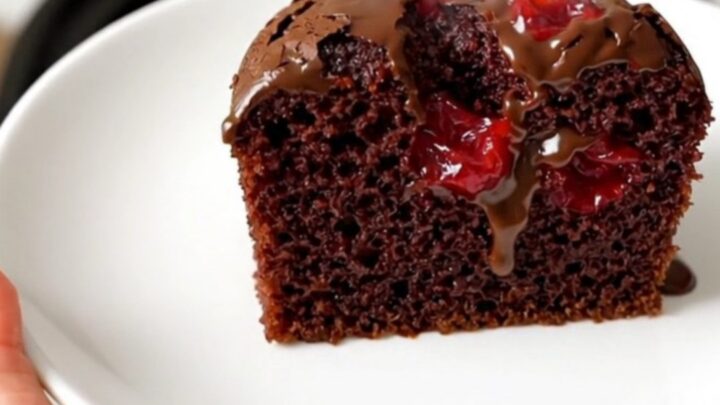 A warm, glossy chocolate cherry dump cake in a black slow cooker on a white quartz countertop.