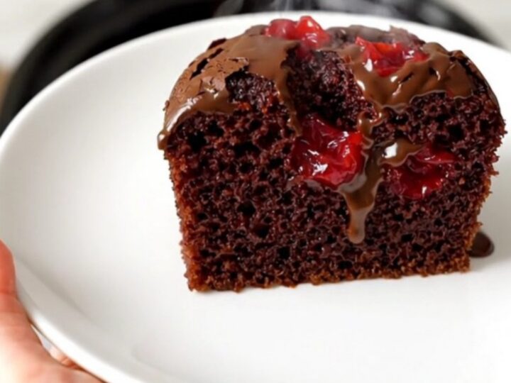 A warm, glossy chocolate cherry dump cake in a black slow cooker on a white quartz countertop.