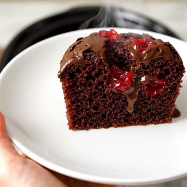 A warm, glossy chocolate cherry dump cake in a black slow cooker on a white quartz countertop.