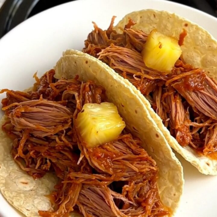A close-up of tender, shredded al pastor pork with pineapple and red onion, served on warm corn tortillas.