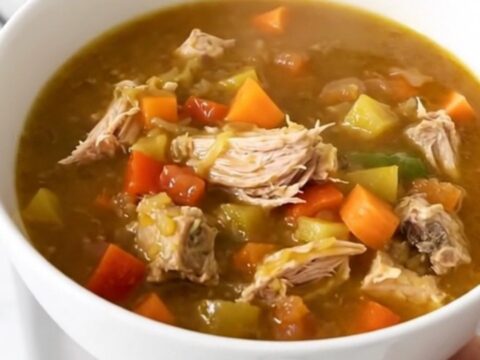 A top-down view of a black slow cooker filled with turkey, sweet potatoes, carrots, and broth.