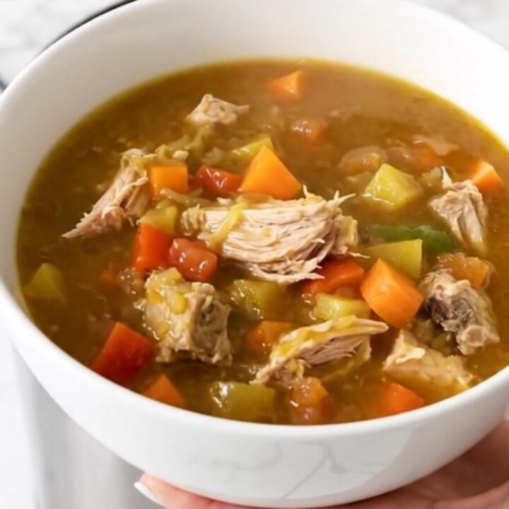 A top-down view of a black slow cooker filled with turkey, sweet potatoes, carrots, and broth.