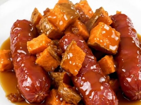 A slow cooker filled with sliced kielbasa and cubed sweet potatoes glazed in a maple butter sauce.