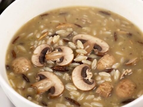 A steaming bowl of creamy wild rice and mushroom soup in a white bowl on a wooden table.