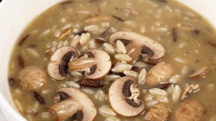 A steaming bowl of creamy wild rice and mushroom soup in a white bowl on a wooden table.