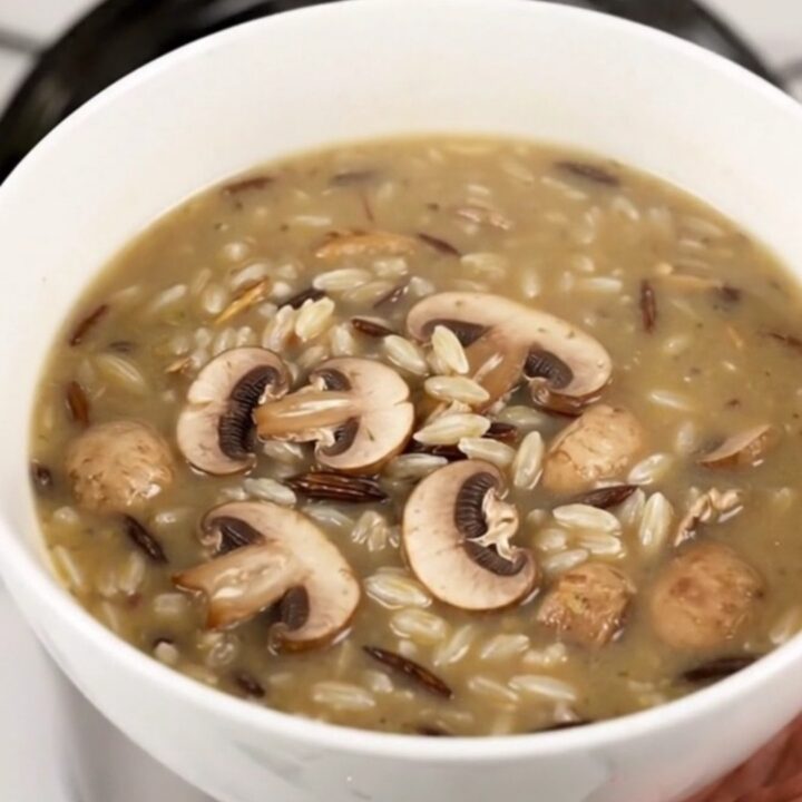 A steaming bowl of creamy wild rice and mushroom soup in a white bowl on a wooden table.