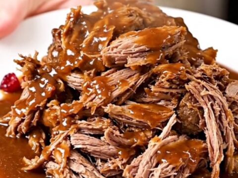 A close-up of tender, shredded beef pot roast in a rich, glossy cranberry-chili sauce on a white plate.