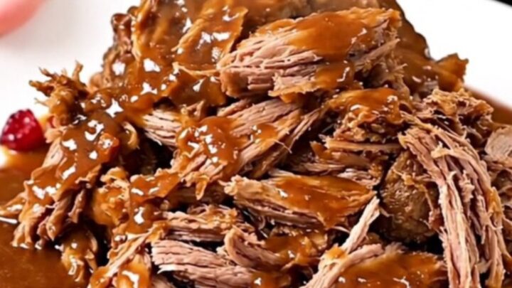 A close-up of tender, shredded beef pot roast in a rich, glossy cranberry-chili sauce on a white plate.