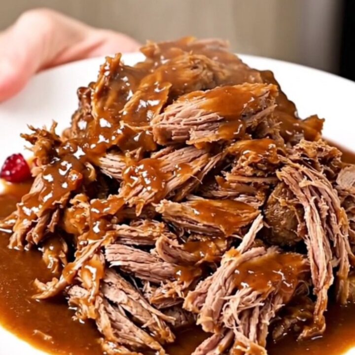 A close-up of tender, shredded beef pot roast in a rich, glossy cranberry-chili sauce on a white plate.