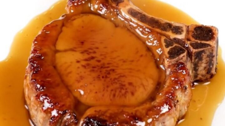 A close-up of a tender, glazed pork chop served on a white plate with a glossy maple mustard finish.