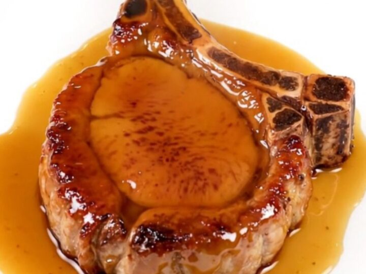 A close-up of a tender, glazed pork chop served on a white plate with a glossy maple mustard finish.