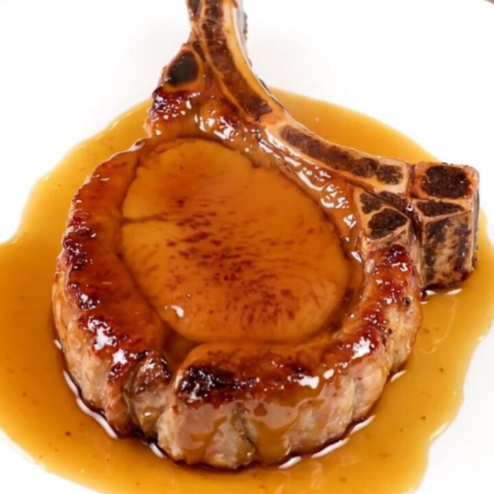 A close-up of a tender, glazed pork chop served on a white plate with a glossy maple mustard finish.