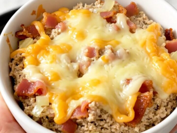 A warm, creamy bacon swiss dip in a white bowl, showing melted cheese and bacon bits.