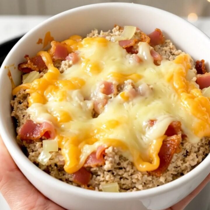 A warm, creamy bacon swiss dip in a white bowl, showing melted cheese and bacon bits.