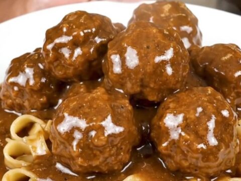A close-up overhead view of Swedish meatballs in a creamy brown mushroom gravy in a black slow cooker.
