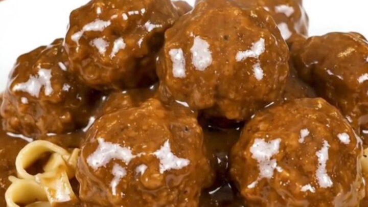 A close-up overhead view of Swedish meatballs in a creamy brown mushroom gravy in a black slow cooker.