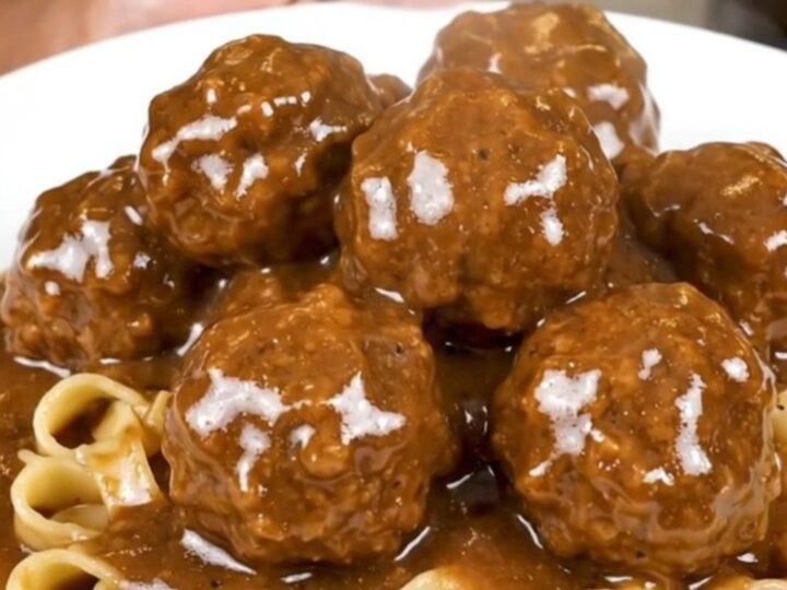 A close-up overhead view of Swedish meatballs in a creamy brown mushroom gravy in a black slow cooker.