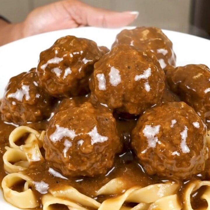 A close-up overhead view of Swedish meatballs in a creamy brown mushroom gravy in a black slow cooker.