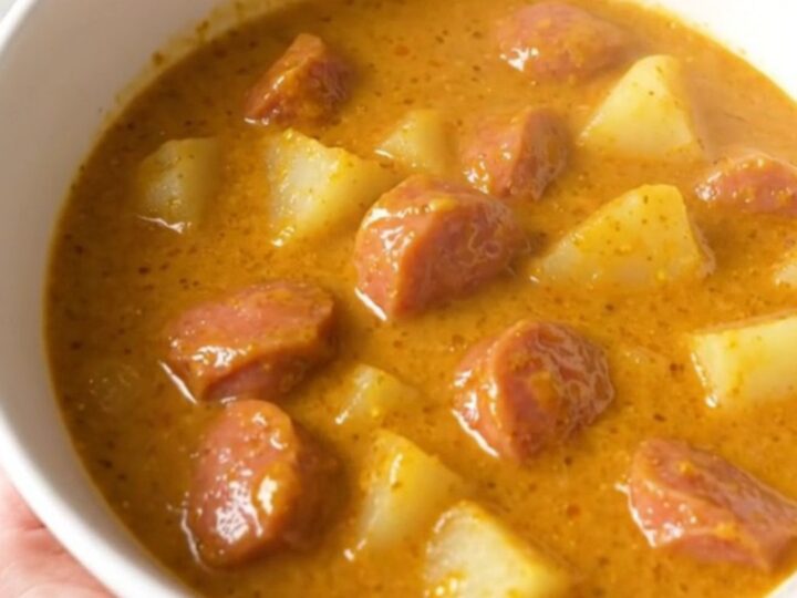 A steaming bowl of creamy bratwurst chowder with visible potato chunks and sausage rounds.