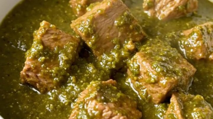A white bowl filled with steaming, tender pork chunks in a glossy green chile verde sauce.