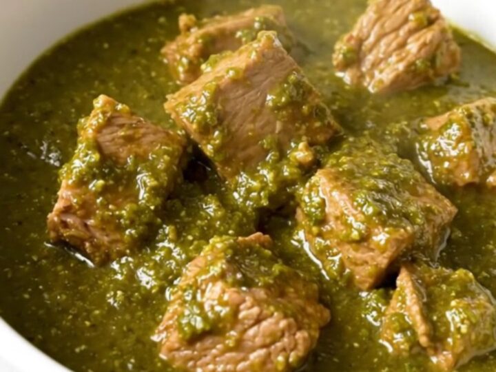 A white bowl filled with steaming, tender pork chunks in a glossy green chile verde sauce.